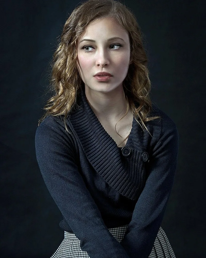 A woman in a dark cardigan against a dark background.