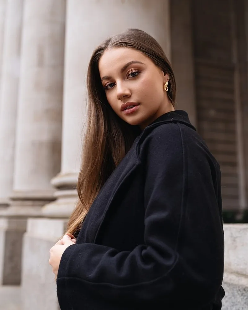 A woman in a long black knit coat beside stone columns.