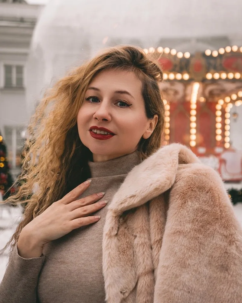 A woman in a pale fur-trimmed coat at night.