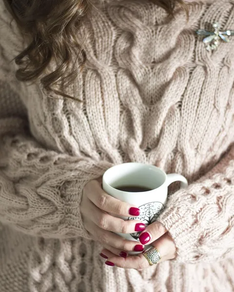 Hands holding a mug against a cream cable knit.