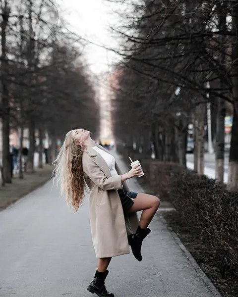A woman in a trench coat and watch walking a city street.
