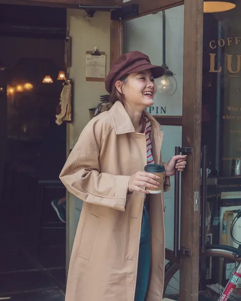 A woman in a tan trench coat on a city street.
