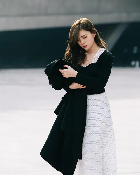 A woman in a long black blazer standing against a pale wall.