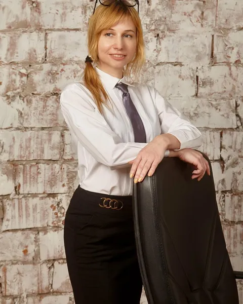 A woman in a white shirt and tie leaning against a brick wall.
