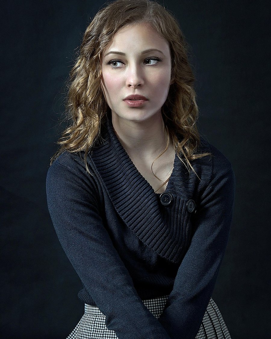 A woman in a dark cardigan against a dark background.