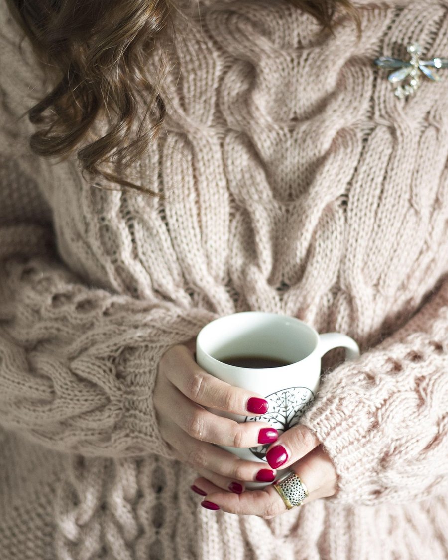 Hands holding a mug against a cream cable knit.