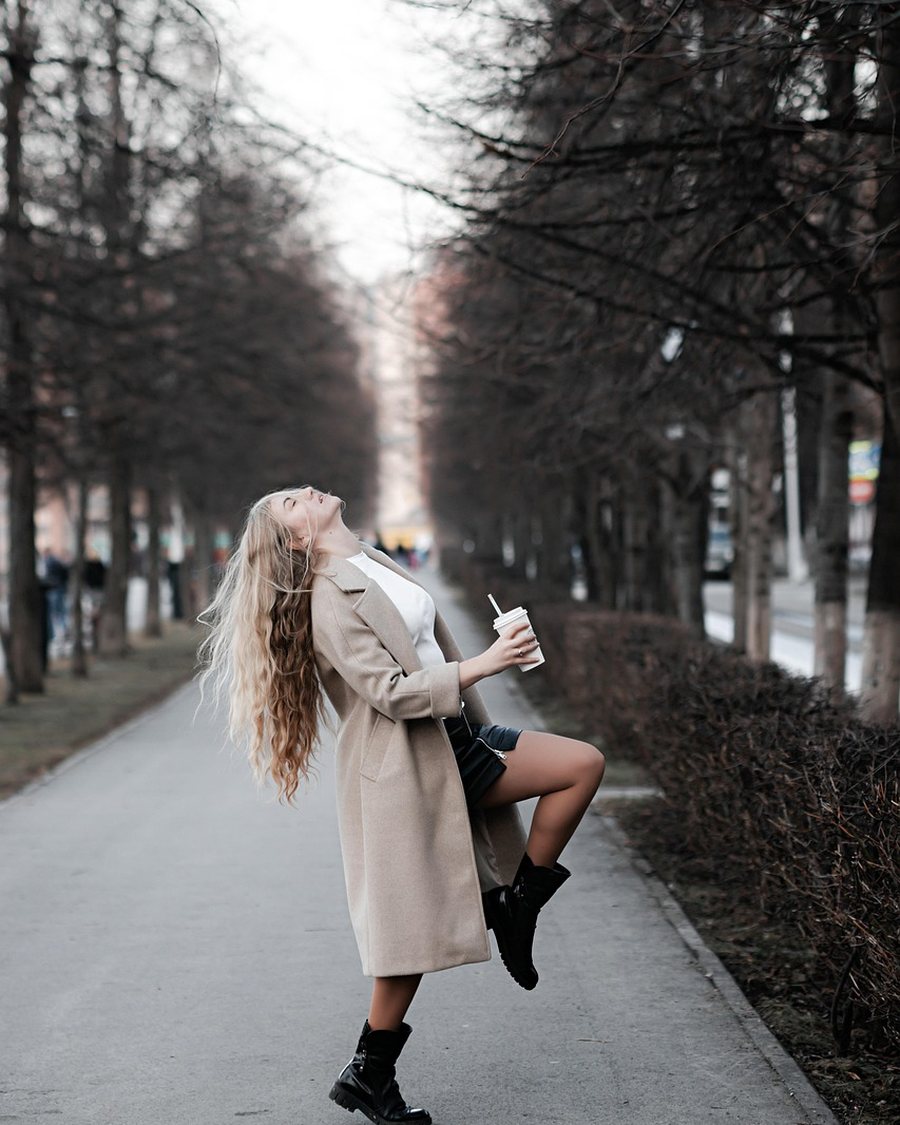 A woman in a trench coat and watch walking a city street.