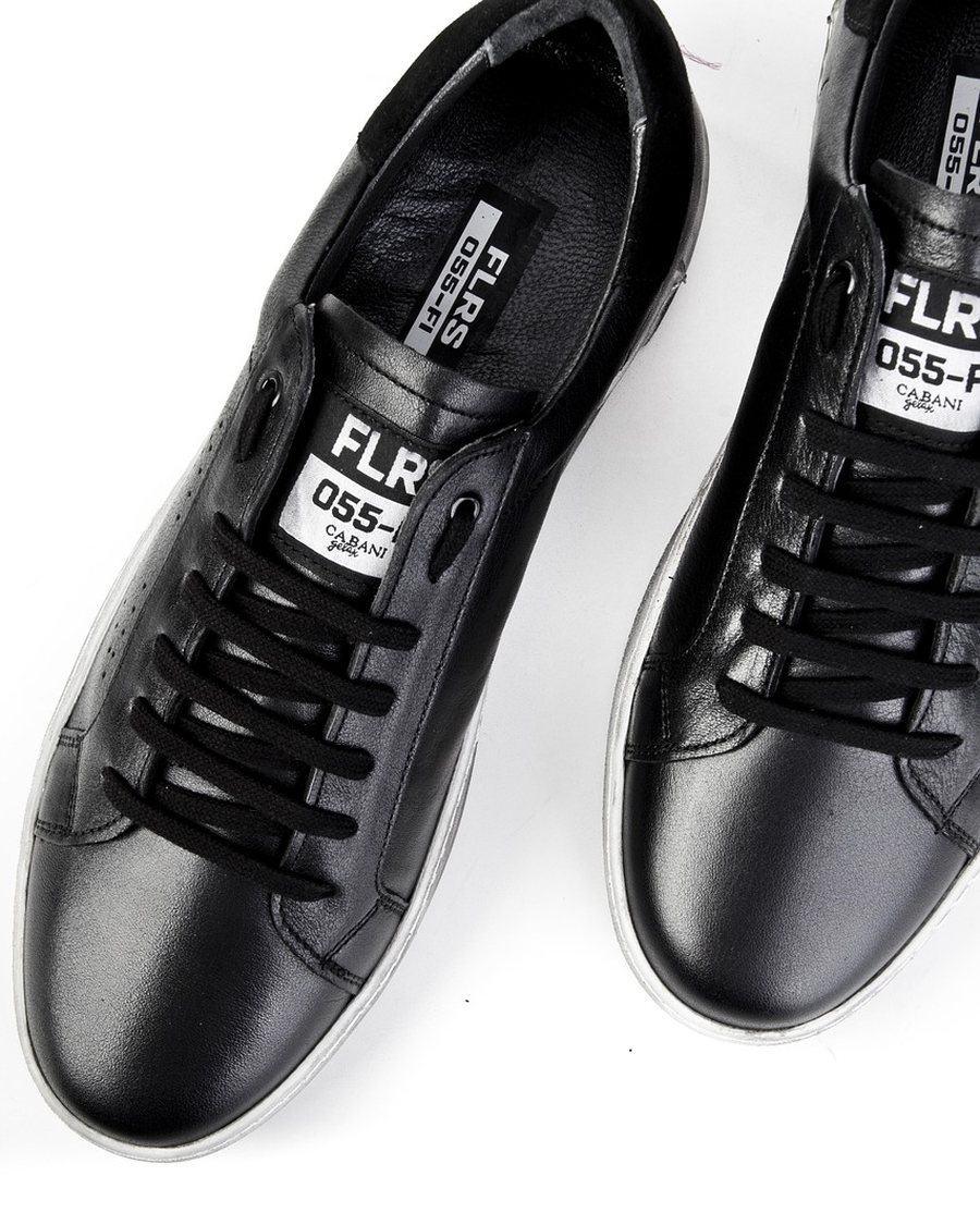 Black leather sneakers photographed on a white surface.